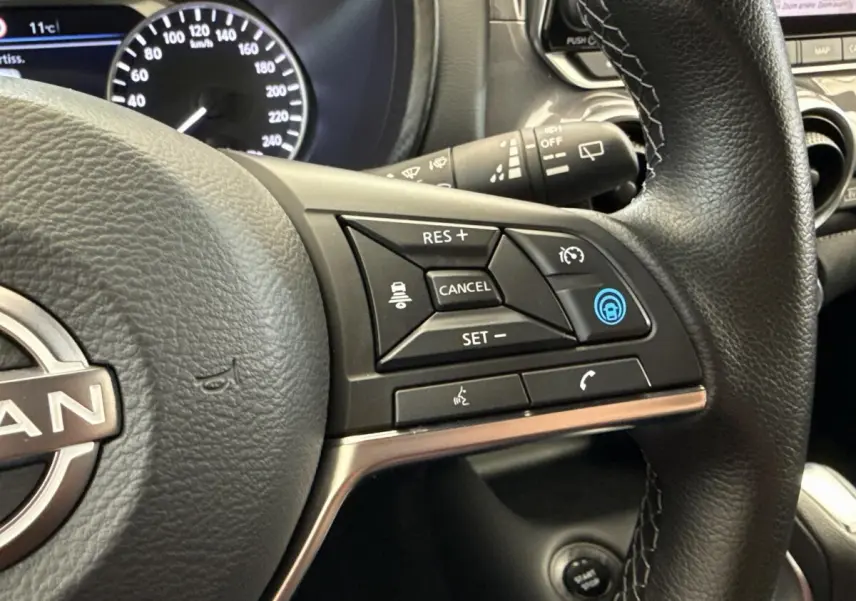 Gros plan sur le volant noir du Nissan Juke 2023, montrant les commandes du régulateur de vitesse et assistance au freinage.