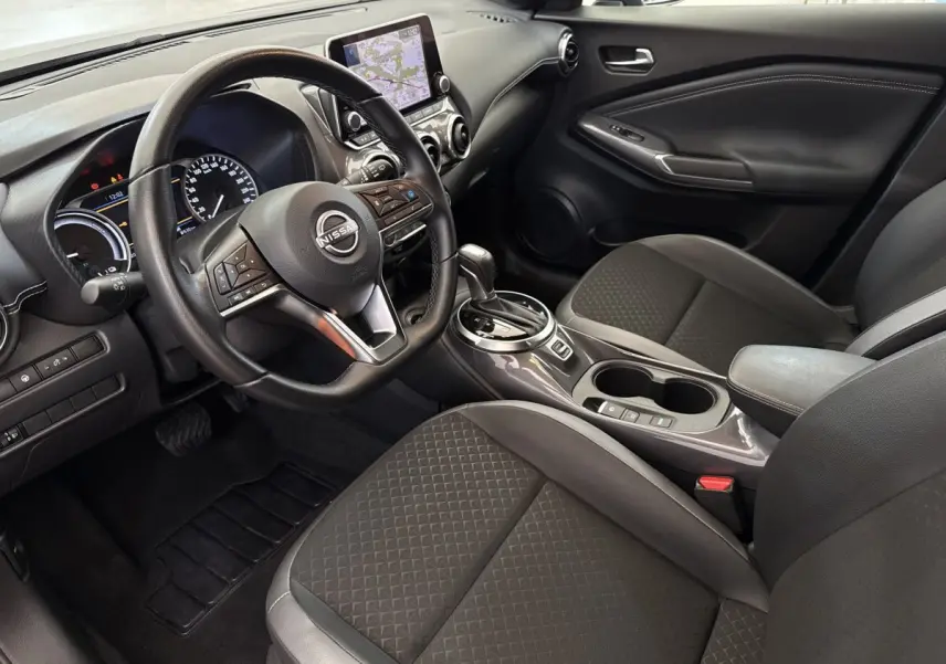 Intérieur du Nissan Juke 2023 vu côté conducteur, montrant volant multifonctions, écran tactile et sièges tissu gris foncé.