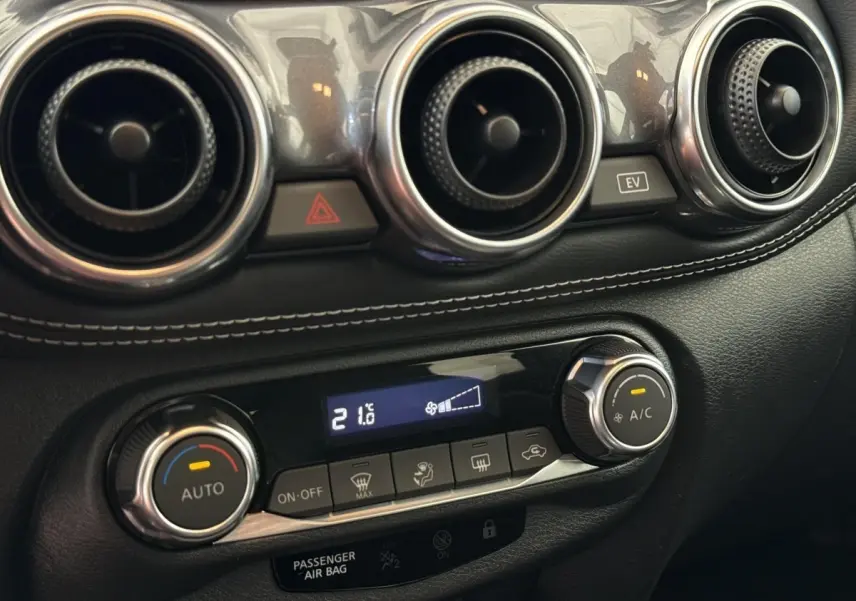 Détail du tableau de bord noir du Nissan Juke 2023 montrant les aérateurs ronds et la commande de climatisation digitale à 21,6°C.