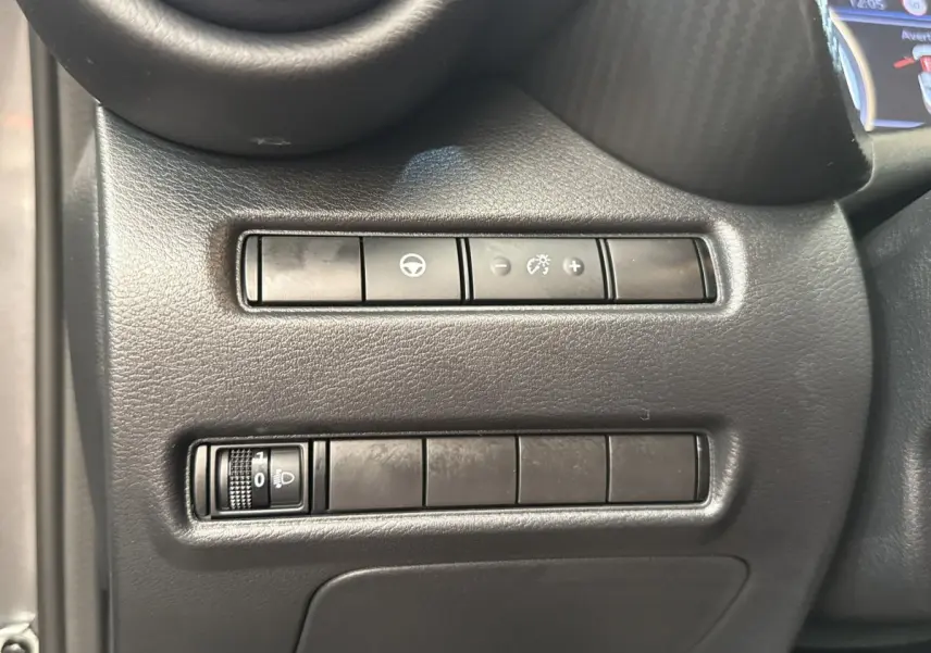 Détail des commandes de réglage des phares et tableau de bord côté conducteur dans un Nissan Juke gris foncé 2023.