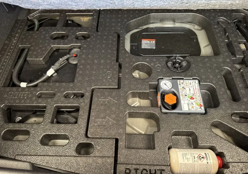Vue rapprochée du coffre du Nissan Juke 2023 gris foncé, montrant le rangement mousse et le kit de réparation pneus.