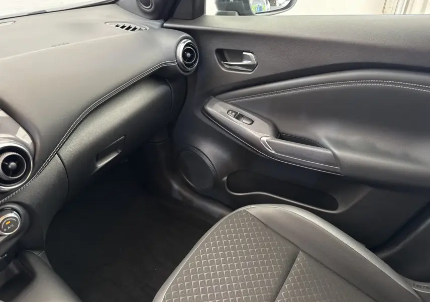 Vue intérieure côté passager du Nissan Juke 2023 gris foncé, avec tableau de bord et porte en cuir noir.