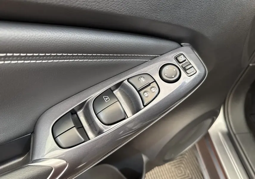 Gros plan sur la commande des vitres et rétroviseurs côté conducteur du Nissan Juke gris foncé 2023.