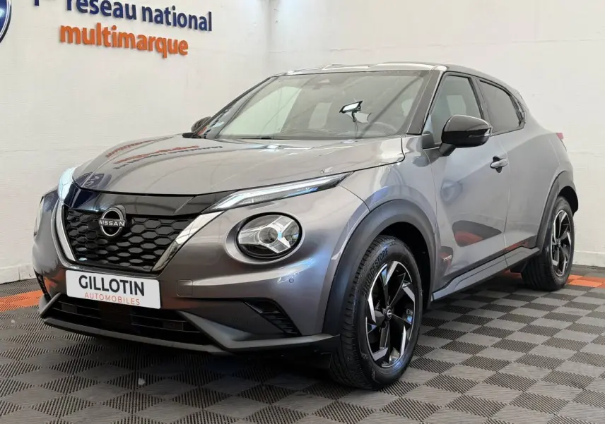 Nissan Juke gris foncé vue 3/4 avant droit, avec calandre noire et jantes alliage bicolores.