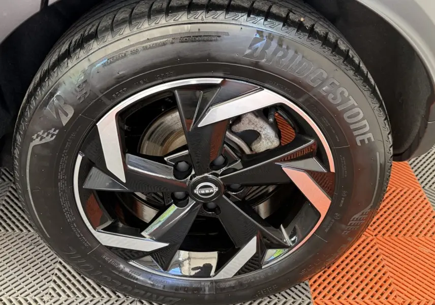 Gros plan sur la roue avant droite d’un Nissan Juke gris foncé, jante alliage noire et argentée au design anguleux.