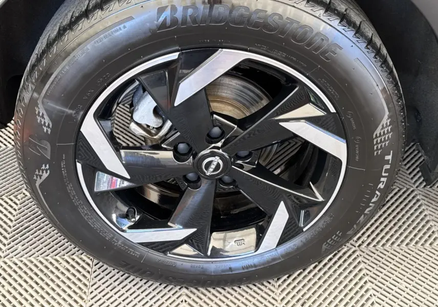 Gros plan sur la roue avant droite du Nissan Juke 2023 gris foncé, jante alliage noir et argent avec pneu Bridgestone.