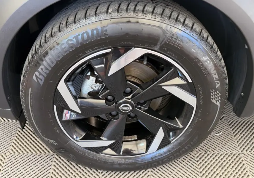 Gros plan sur la roue avant droite d’un Nissan Juke gris foncé, jante alliage noire et argentée, pneu Bridgestone.