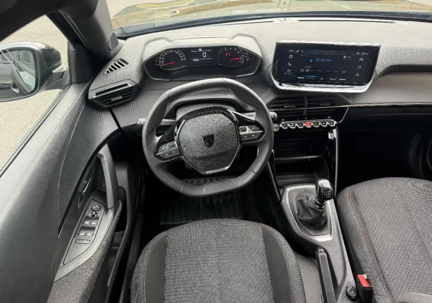 Vue intérieure frontale du Peugeot 2008 noir perla 2025, mettant en valeur le volant compact, la boîte manuelle et l'écran tactile central.