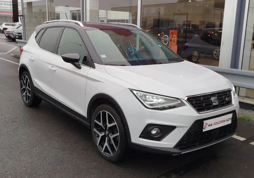 SEAT Arona blanc avec toit gris magnétique, vue 3/4 avant droit, feux allumés et jantes alliage noires.