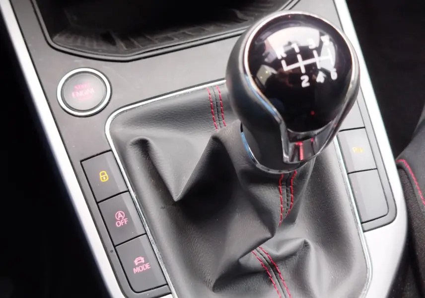 Gros plan sur le levier de vitesses manuel avec surpiqûres rouges et bouton start/stop dans l’habitacle du SEAT Arona.