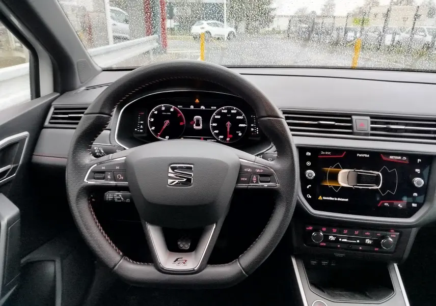 Vue intérieure centrée sur le volant FR de la SEAT Arona blanc, tableau de bord et écran tactile avec aide au stationnement.