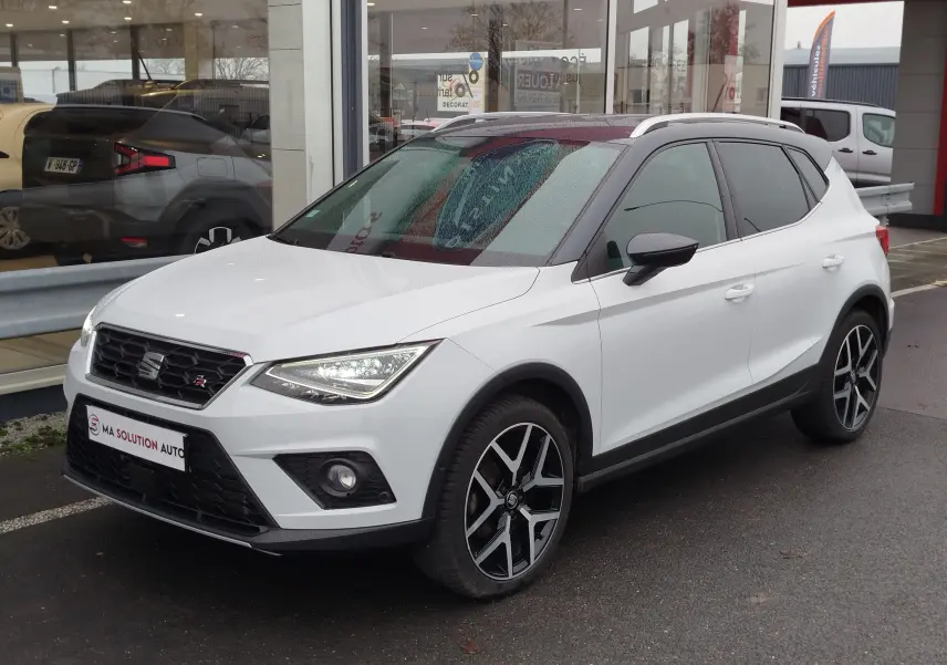 SEAT Arona blanc avec toit gris magnétique, vue 3/4 avant droit, jantes alliage noires et phares allumés.