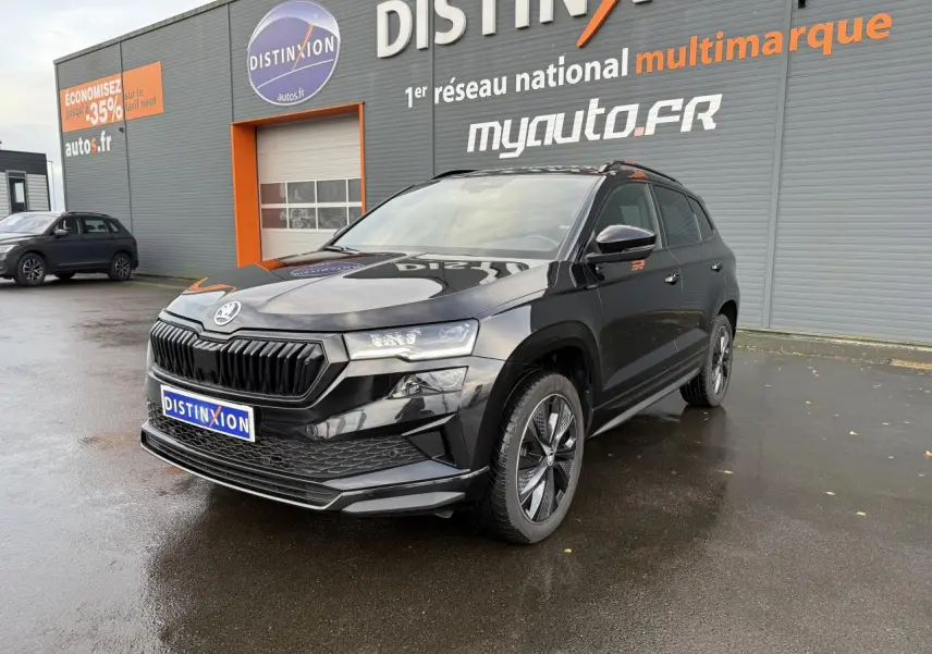 Vue 3/4 avant d'un Skoda Karoq noir Magic nacré avec jantes alliage et calandre noire devant un bâtiment Distinxion.