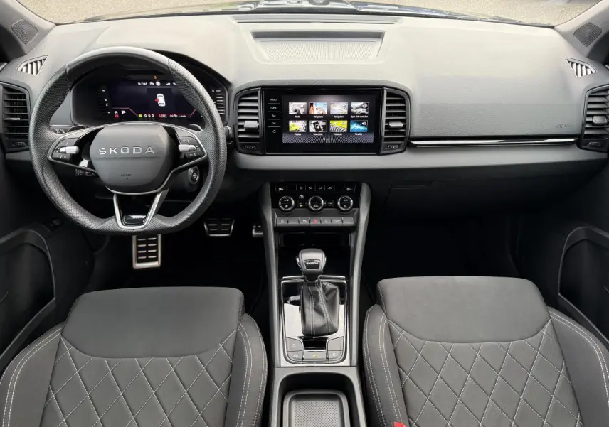 Intérieur noir du Skoda Karoq 2025, vue frontale sur le tableau de bord, volant sport et console centrale avec écran tactile.
