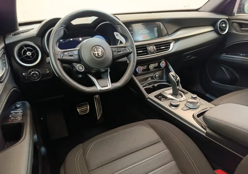 Intérieur noir de l'Alfa Romeo Stelvio 2024, vue côté conducteur sur volant, tableau de bord et console centrale.