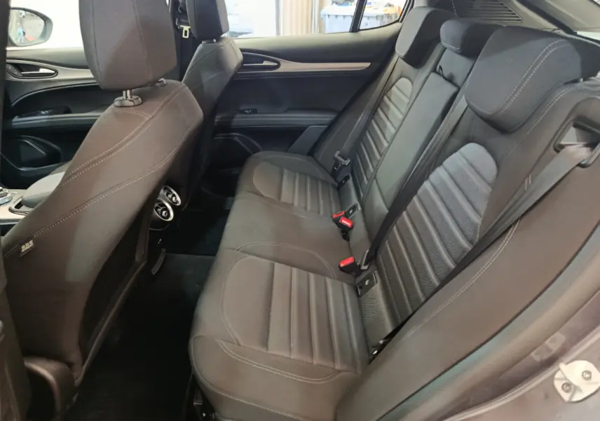 Intérieur arrière côté droit de l'Alfa Romeo Stelvio gris foncé, montrant les sièges en tissu et les aérateurs centraux.