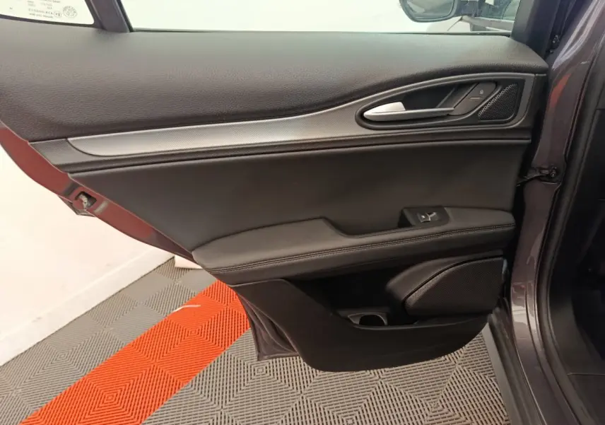 Porte côté gauche ouverte d'un Alfa Romeo Stelvio gris foncé, montrant la garniture intérieure noire avec poignée alu.