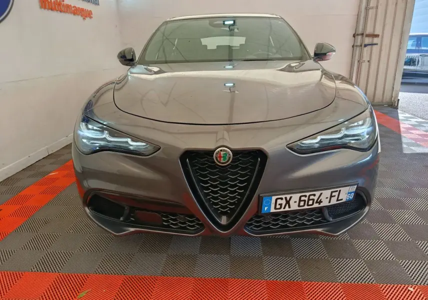 Vue frontale d'un Alfa Romeo Stelvio gris foncé avec calandre triangulaire et phares LED allumés.