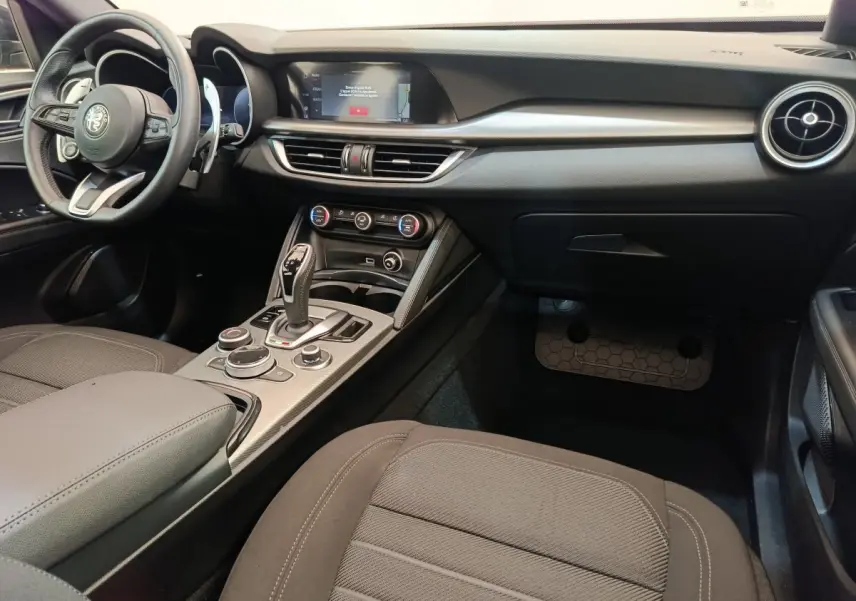 Intérieur de l'Alfa Romeo Stelvio 2024 vu côté passager, avec tableau de bord noir et console centrale moderne.