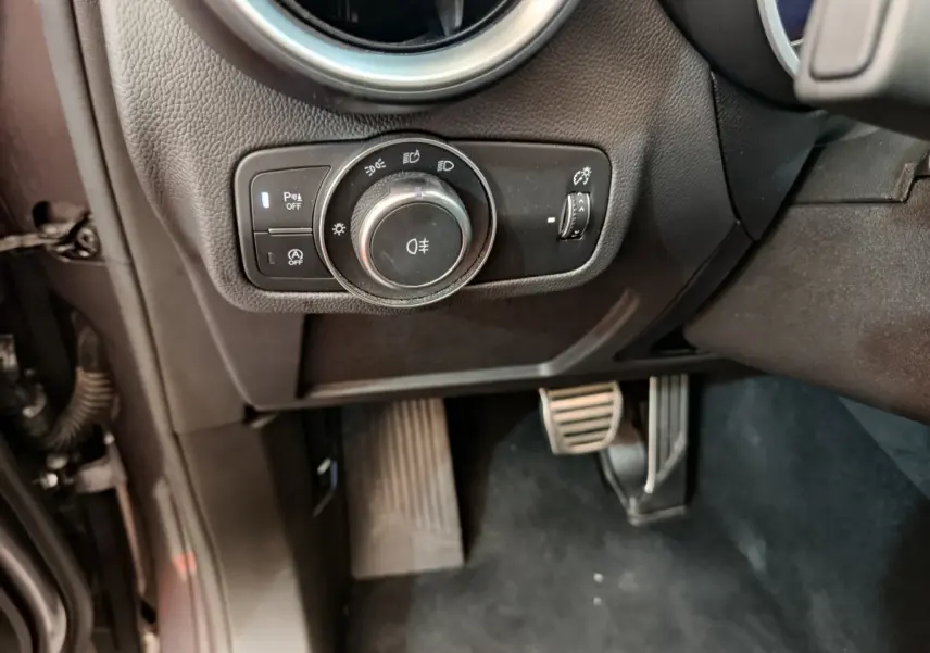 Gros plan sur la commande des phares et les pédales côté gauche de l'Alfa Romeo Stelvio gris foncé 2024 Sprint.