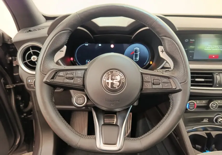 Vue rapprochée du volant cuir noir de l'Alfa Romeo Stelvio 2024 avec tableau de bord digital et commandes intégrées.