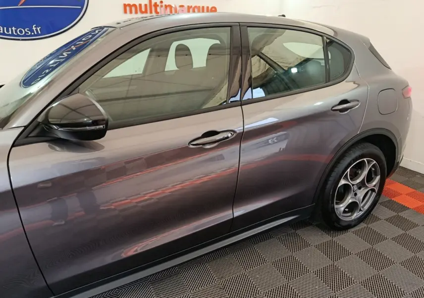 Vue côté gauche de l'Alfa Romeo Stelvio gris foncé mettant en valeur ses jantes distinctives et la ligne de caisse fluide.