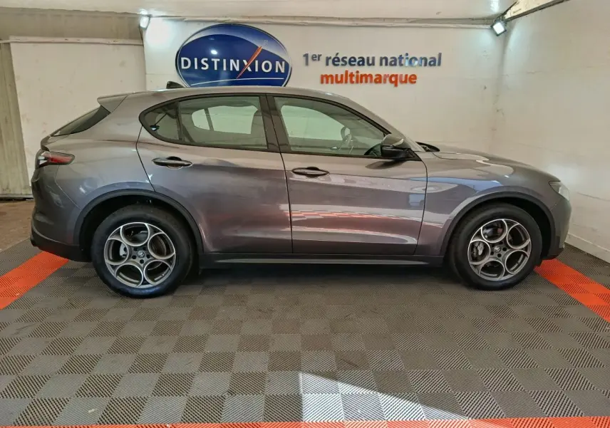 Vue de profil côté gauche d'un Alfa Romeo Stelvio gris foncé 2024 dans un showroom multimarque.