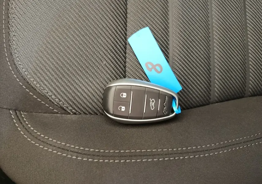 Gros plan sur la clé noire avec étiquette bleue posée sur un siège tissu gris foncé de l'Alfa Romeo Stelvio.