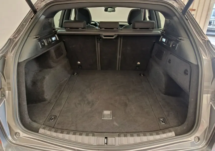 Coffre ouvert vu de l'arrière d'un Alfa Romeo Stelvio gris foncé, intérieur spacieux et tapis noir.