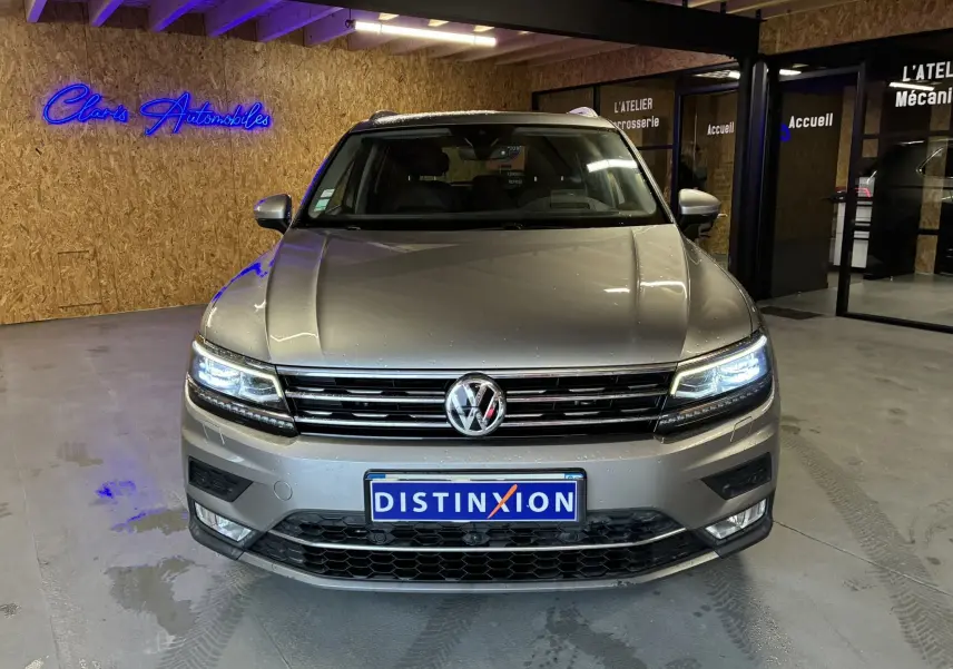 Volkswagen Tiguan gris 2.0 TDI 150 Carat vu de face, phares allumés, dans un garage avec enseigne néon bleue.