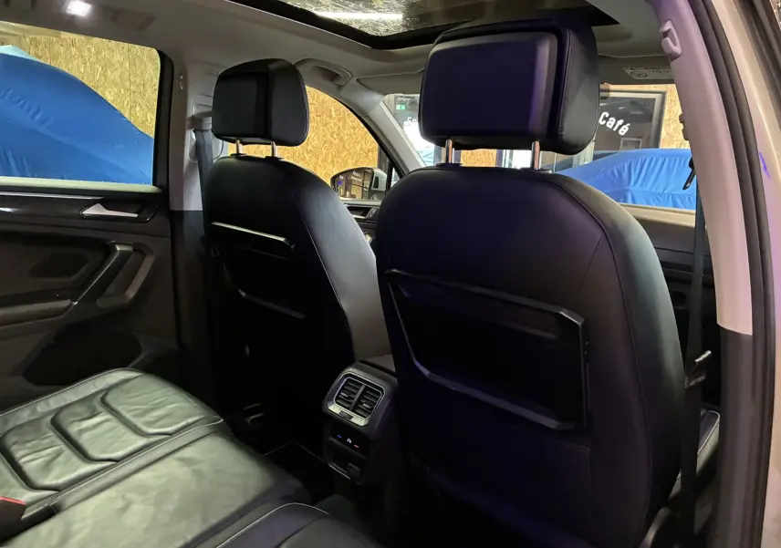 Vue intérieure arrière du Volkswagen Tiguan 2.0 TDI gris, montrant les sièges en cuir noir et les aérateurs centraux.