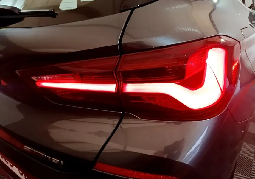 Gros plan sur le feu arrière droit allumé d'une BMW X2 sDrive18i Lounge gris foncé, soulignant les lignes modernes du véhicule.