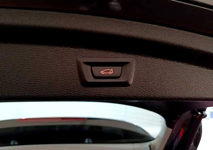 Gros plan sur le bouton d'ouverture électrique du coffre du BMW X2 sDrive18i Lounge DKG7 gris foncé, vue intérieure arrière.