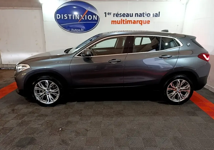 BMW X2 sDrive18i Lounge gris foncé vue de profil côté gauche, avec jantes alliage et logo BMW sur l'aile arrière.