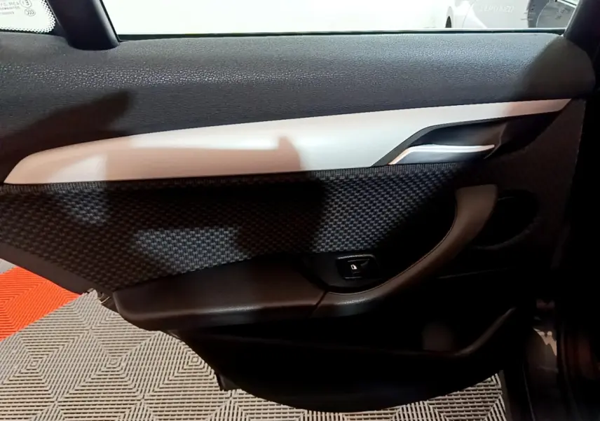 Vue intérieure du panneau de porte côté droit de BMW X2 gris foncé, avec poignée argentée et bouton de verrouillage.