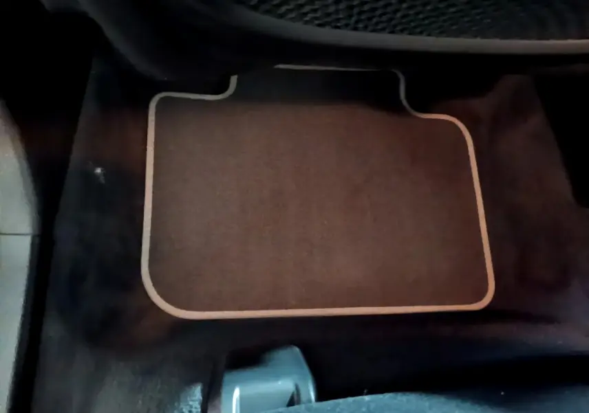 Tapis de sol beige sur fond noir, vue rapprochée de l'intérieur côté passager d'une BMW X2 gris foncé.