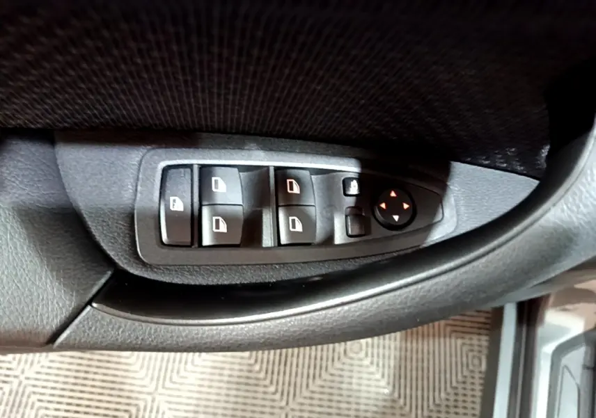Gros plan sur les commandes des vitres et rétroviseurs côté gauche d’une BMW X2 gris foncé 2021.