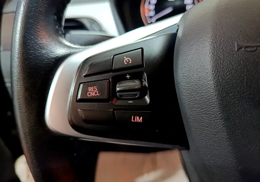 Gros plan sur les commandes du régulateur de vitesse au volant cuir d’une BMW X2 sDrive18i Lounge gris foncé.