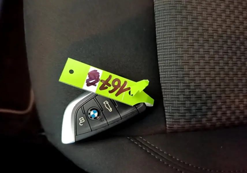 Clé de voiture BMW posée sur un siège en tissu gris foncé, avec un porte-étiquette vert fluo.