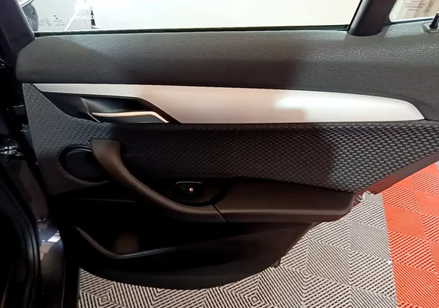 Vue intérieure du panneau de porte arrière gauche du BMW X2 sDrive18i Lounge gris foncé avec habillage texturé et insert argenté.