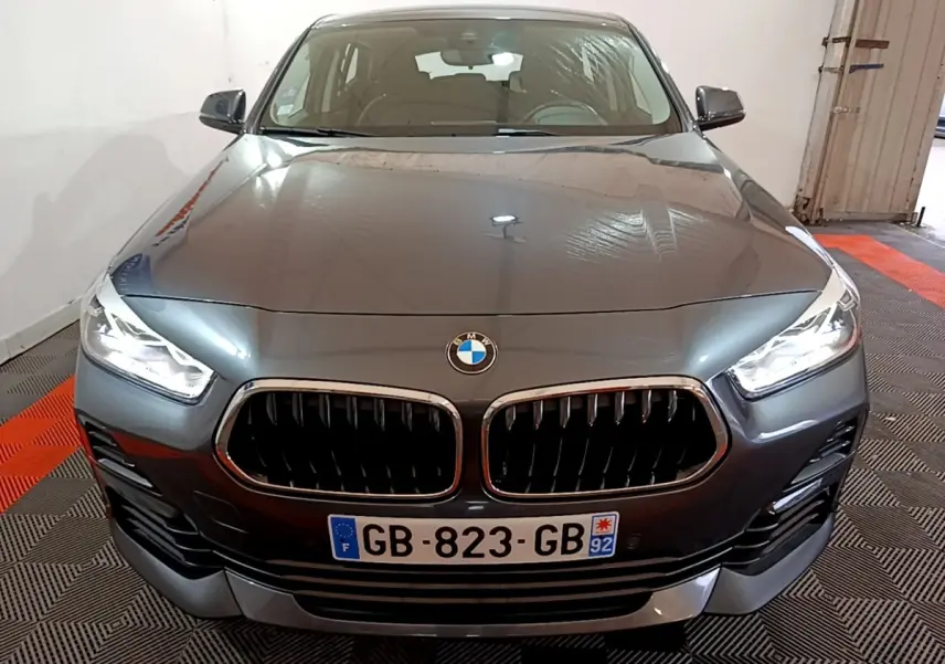 Vue frontale d'une BMW X2 sDrive18i Lounge DKG7 gris foncé avec calandre double haricot et phares LED allumés.
