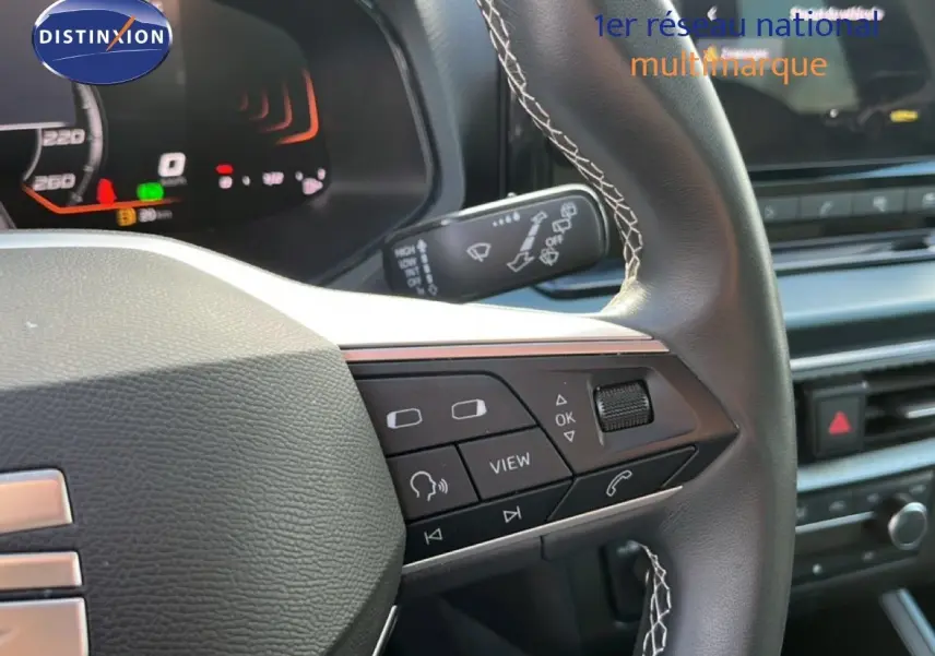 Gros plan sur le volant cuir noir avec surpiqûres blanches du SEAT Arona 2025, montrant les commandes multifonctions.