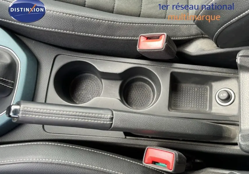 Vue rapprochée de la console centrale du SEAT Arona 2025, montrant le frein à main, porte-gobelets et bouton 12V en noir.