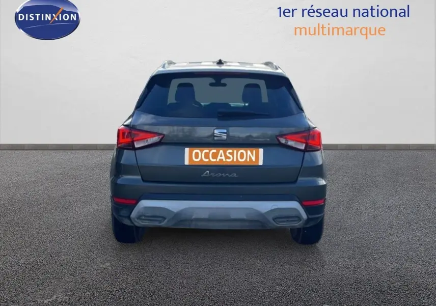 Vue arrière d'un SEAT Arona gris métallique avec toit noir, immatriculé "OCCASION" sur un sol goudronné.