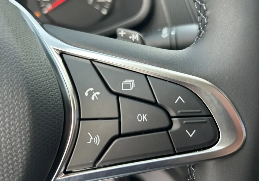 Gros plan sur les commandes multifonctions au volant côté droit du Renault Trafic Fourgon blanc, boutons noirs avec contour chromé.