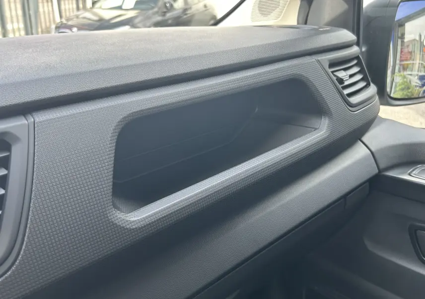 Détail intérieur du tableau de bord noir du Renault Trafic Fourgon, avec vide-poches et aérateurs visibles côté passager.