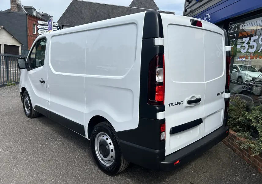 Renault Trafic Fourgon blanc vu en 3/4 arrière droit, avec porte latérale coulissante et feux arrière verticaux.