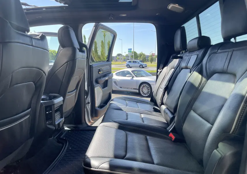 Intérieur arrière du Dodge RAM 1500 blanc nacré, sièges cuir noir et porte arrière gauche ouverte sur parking.