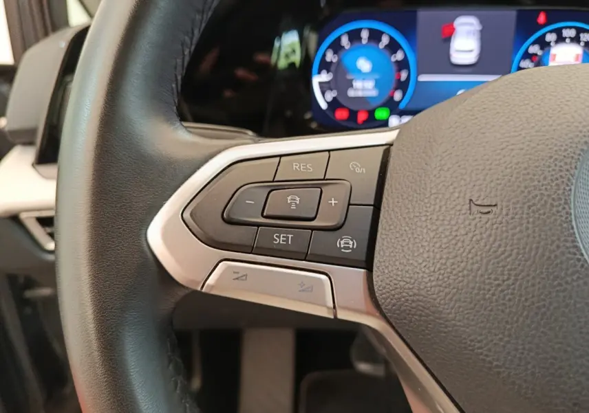 Gros plan sur le côté gauche du volant cuir d'une Volkswagen Golf gris foncé, avec commandes de régulateur adaptatif et tableau de bord numérique.