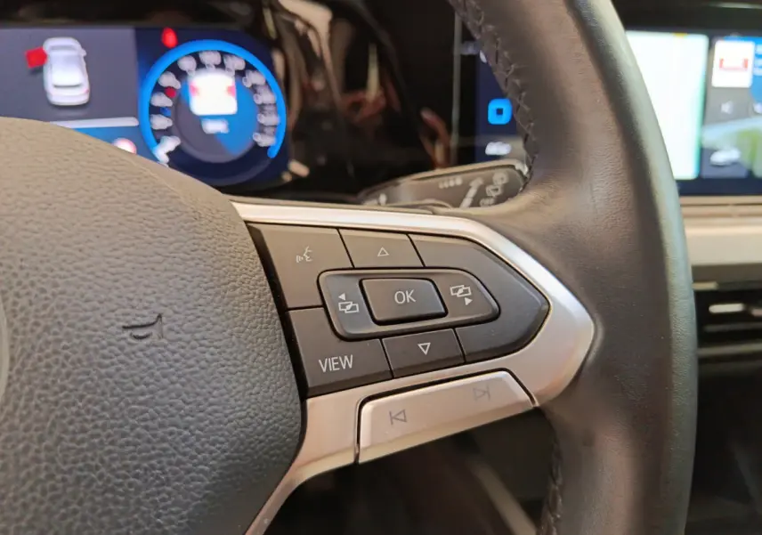 Gros plan sur le côté droit du volant cuir d'une Volkswagen Golf gris foncé, avec commandes multifonctions et tableau de bord numérique.